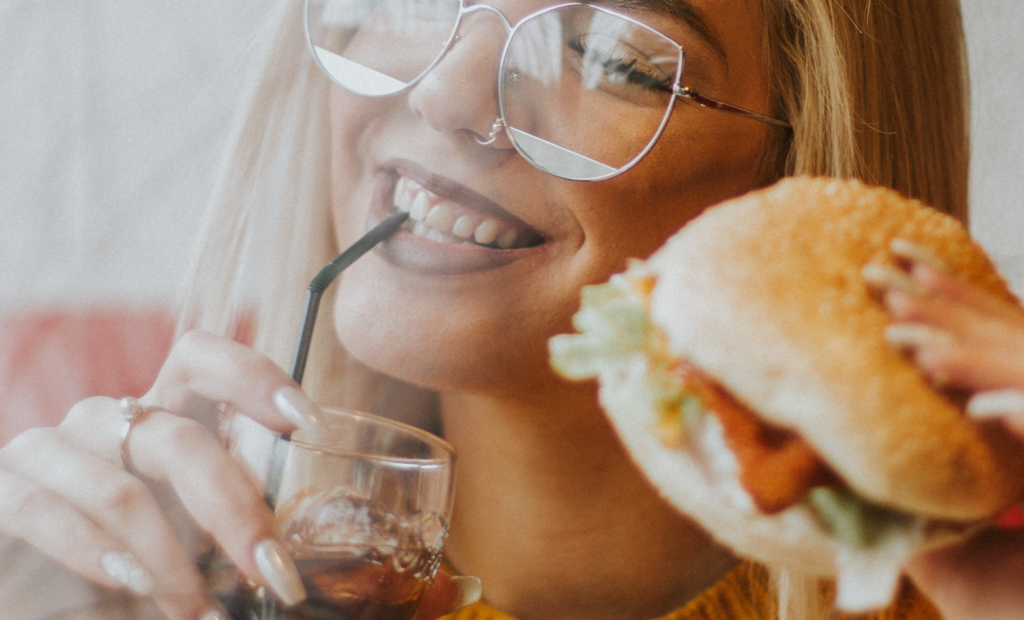 woman holding burger while drinking a cola