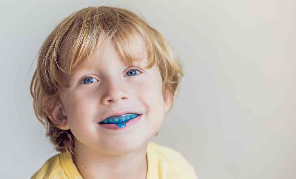 a kid with blue eyes wearing blue invisalign aligner