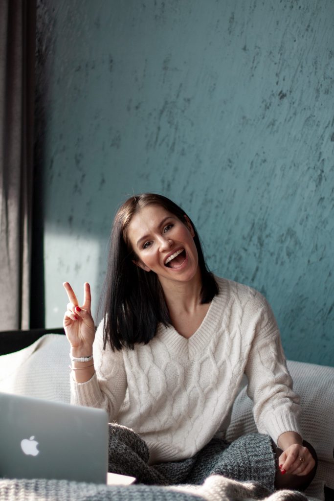 woman with white knit top showing peace sign