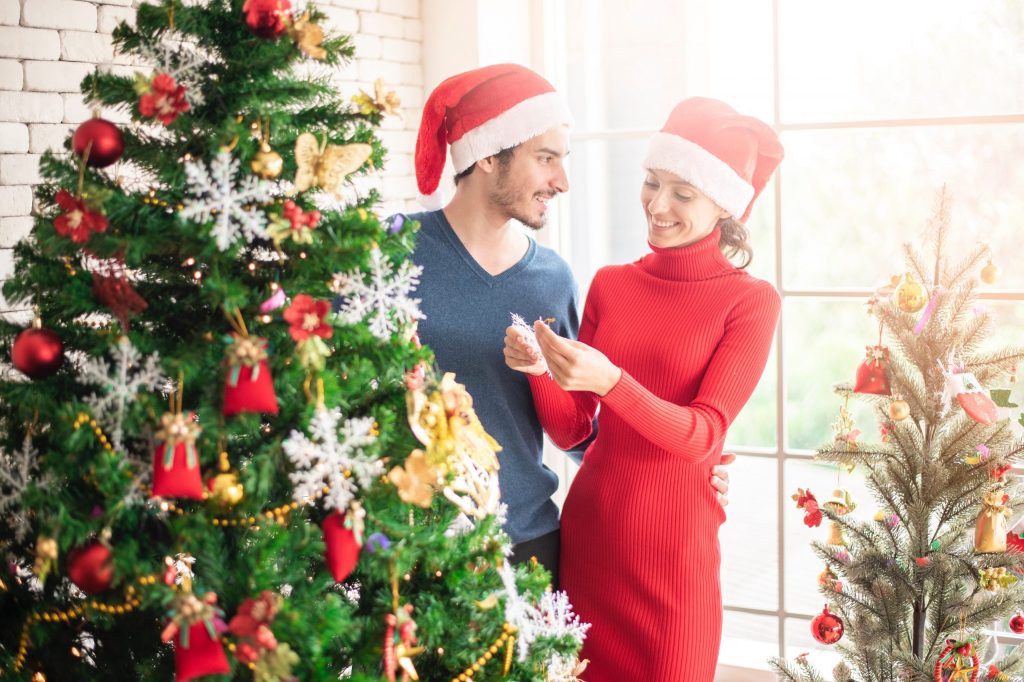a couple standing beside the Christmas tree wearing Santa hat